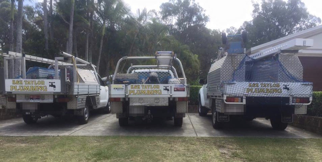 Three white K&K Taylor Plumbing utes lined up in a driveway, each sign-written in gold