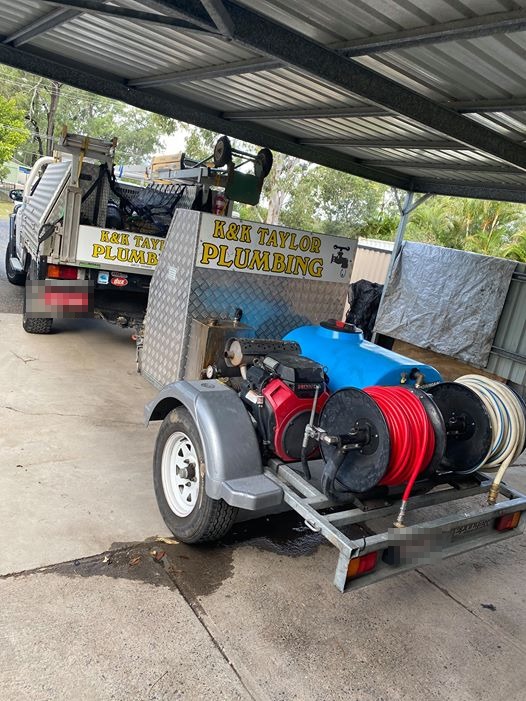 A K&K Taylor Plumbing ute and the jetter trailer with red and white hose reels, parked under a carport